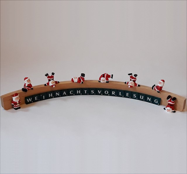 In einem Halbkreis mit Scrabblesteinen gelegtes Wort Weihnachtsvorlesung, auf dem einige Weihnachtsmänner herumtoben