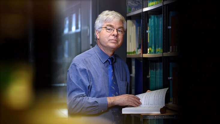 Detlef Stammer in einer Bibliothek mit einem Buch in der Hand.