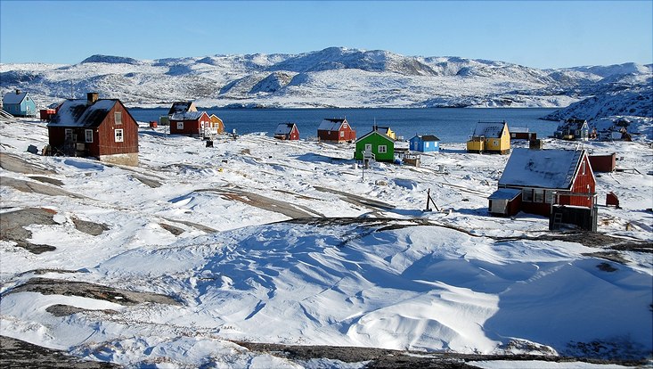Dorf in Grünland umgeben von Schnee, See im Hintergrund