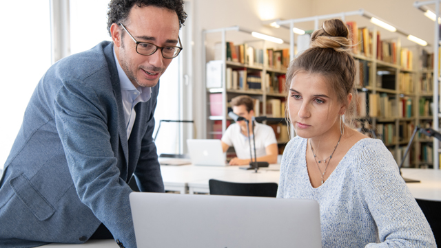Mann zeigt Studierenden etwas am Bildschirm eines Laptops