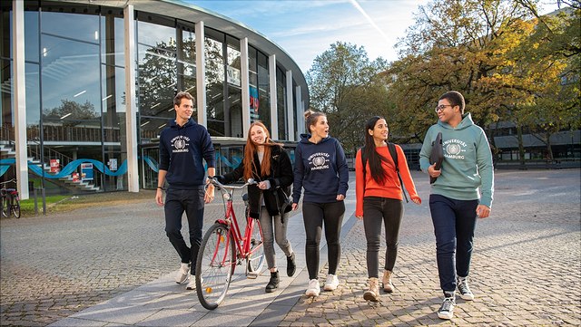 Studierende schlendern über den Hauptcampus am Audimax-Gebäude vorbei.