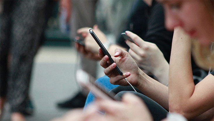 line up of people sitting and scrolling on their smartphone screens