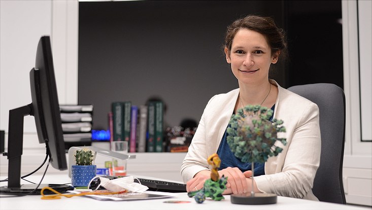 Eine Frau sitzt am Schreibtisch, vor ihr steht ein rundes Modell mit Zacken