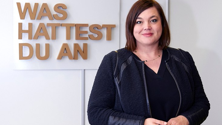 A woman in front of the words "Was hattest du an"