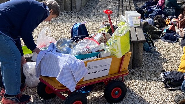 teaser kinderprogramm-640x361 Ein mit allerlei Material beladener Bollerwagen steht mittig im Bild.