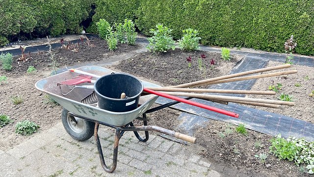 Eine mit Gartengeräten beladene Schubkarre vor einem frisch umgegrabenen Beet