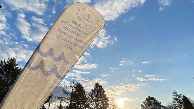 teaser konzert schmidtchen 640x361 weißes Banner mit dem Schriftzug "Café Schmidtchen" ragt in einen blauen Himmel mit weißen Wölkchen