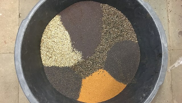 Eine schwarze Maurerbütt gefüllt mit verschiedenfarbigen Saatkörnern