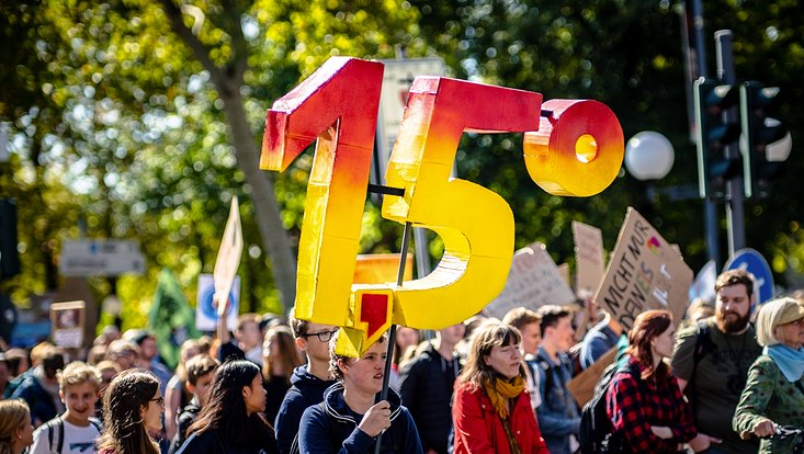 Klimaschutzdemonstrant hält ein 3D Modell von "1,5°" über dem Kopf