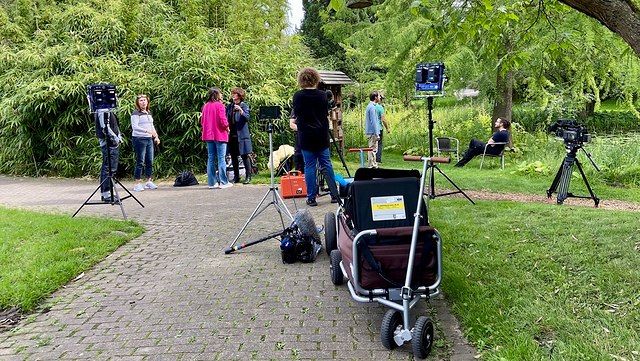 teaser fotoaufnahmen-640x361 (3) ein gepflasterter Weg der in den Bildhintergrund führt. Viele Menschen und einige Kameras stehen herum