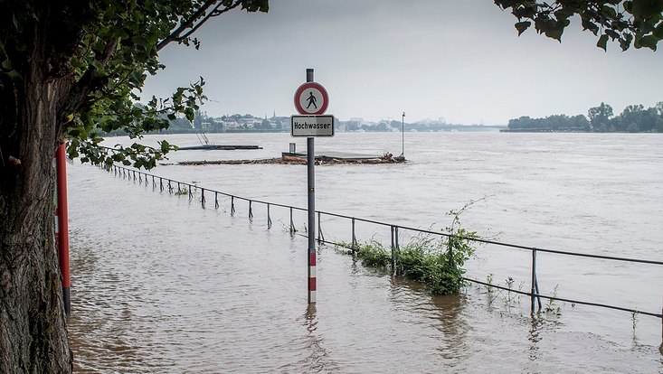 Überflutung, am Ufer steht ein Schild mit dem Wort "Hochwasser".