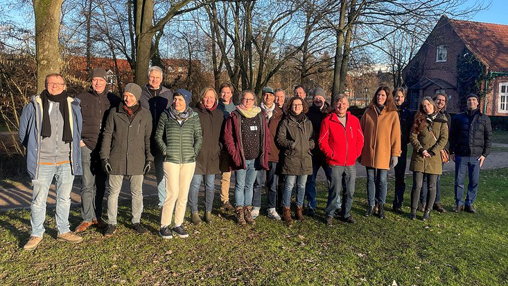 Eine Gruppe von Personen steht auf einer Wiese vor Bäumen