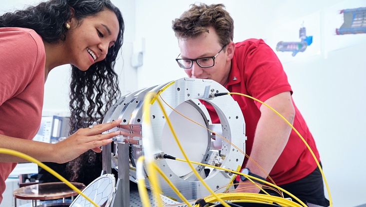 madmax-©jensruessmann-733x414 The MADMAX (Magnetized Disc and Mirror Axion) experiment seeks to detect axion dark matter and the prototype at Hamburg is shown here with QU researchers. This experiment will boost the axion-to-photon conversion signal by employing multiple dielectr