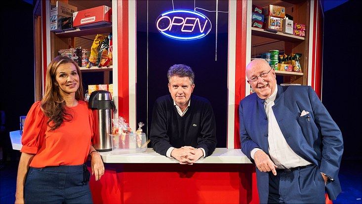Bühnenbild: die drei Moderator:innen vor einer Kiosk-Kulisse