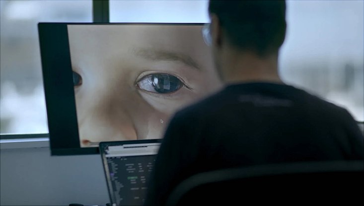 still image from "Eternal you" documentary showing an AI generated image of a baby on a computer screen with an employee sitting in front of it