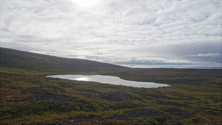View over Blaesedalen with lake in the center and with ocean and icebergs at the horizon