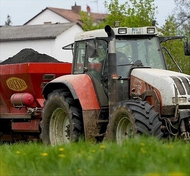 A red tractor spreads rock flour and biochar on the field to remove CO2 from the atmosphere.