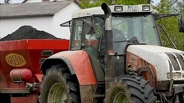 A red tractor spreads rock flour and biochar on the field to remove CO2 from the atmosphere.