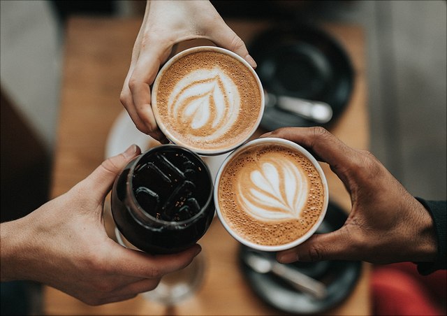 nathan-dumlao-6vhpy27jdps-unsplash-640x452 Drei Personen stoßen mit Kaffeetassen an.