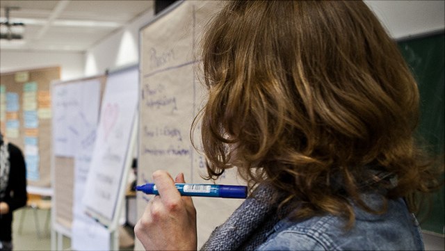 worshop-foto-640x361 Eine Moderatorin steht vor einer Pinnwand und hält einen blauen Stift.