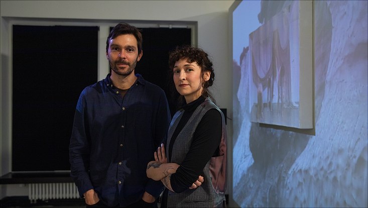bild3 Ein Mann und eine Frau stehen neben einer Leinwand, die einen Film zeigt. Der Film zeigt tanzende Personen.