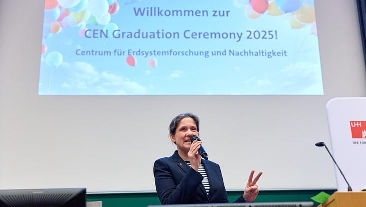2025-02-cen-graduiertenfeier--8278-733x414 Prof. Johanna Baehr hält zwei Finger hoch, sie steht vor der Präsentation mit der Aufschrift "Willkommen zur CEN Graduation Ceremony 2025!"