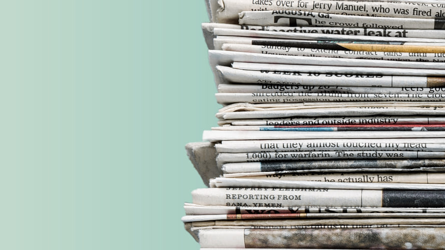 A stack of newspapers in front of a light turquoise background