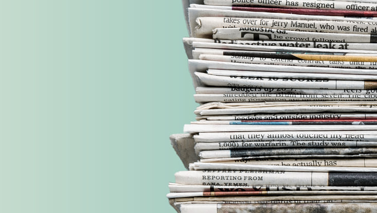 A stack of newspapers in front of a light turquoise background