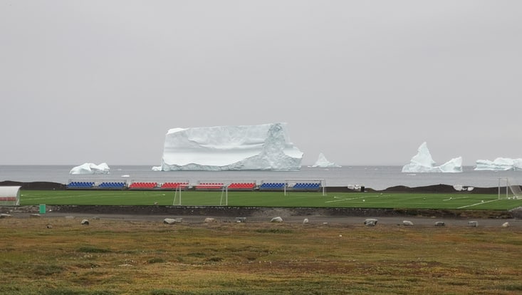 View over the soccer field of Qeqertarsuaq towards the ocean with huge icebergs drifting close by the coast