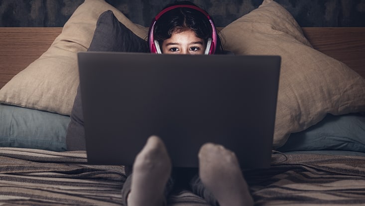 Mädchen mit Computer auf Bett sitzend