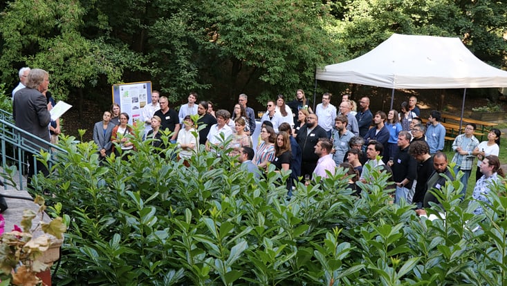 Köppen Slide 4 View into the garden of the location, people listening to a speach