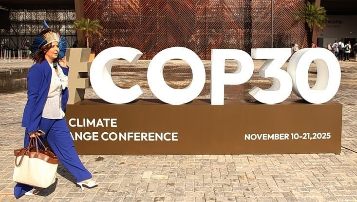 Zu sehen ist eine Person in einem blauen Anzug mit Kopfschmuck. Im Hintergrund ist ein großes COP 30 Zeichen.