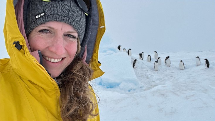 A photo of Stefanie Arndt at an expedition in the antarctic, with penguins in the background.