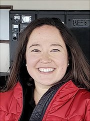 Das Bild ist ein Portrait von Eleanor Frajka-Williams. Eleanor ist eine weiblich gelesene, weiße Person. Eleanor hat glatte braune offene Haare und trägt eine rote Jacke. Eleanor lächelt.