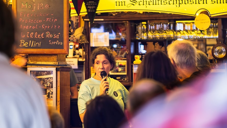 A woman speaks into a microphone at an event in a bar.