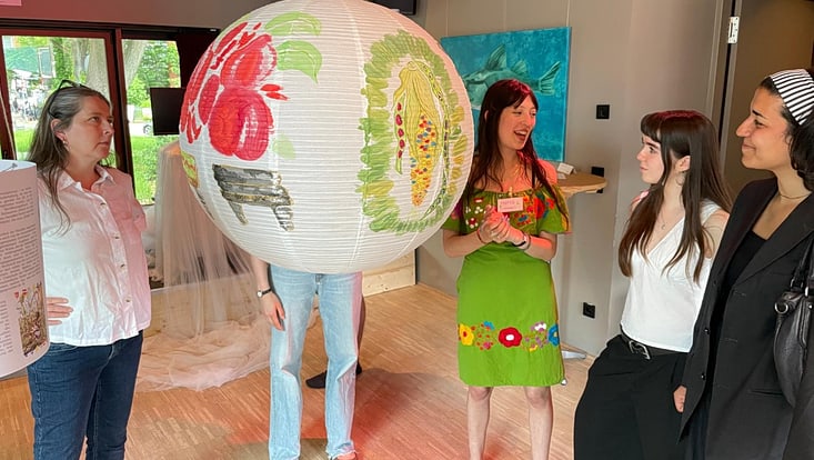 Marla erklärt Besucherinnen ihr Kunstwerk über traditionelle Maya-Anbaumethoden