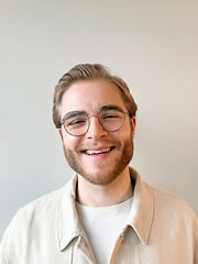 Porträtfoto eines Mannes mit kurzen Haaren und Brille vor einer hellen Wand