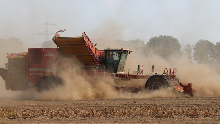 A tractor drives across dry ground, kicking up dust