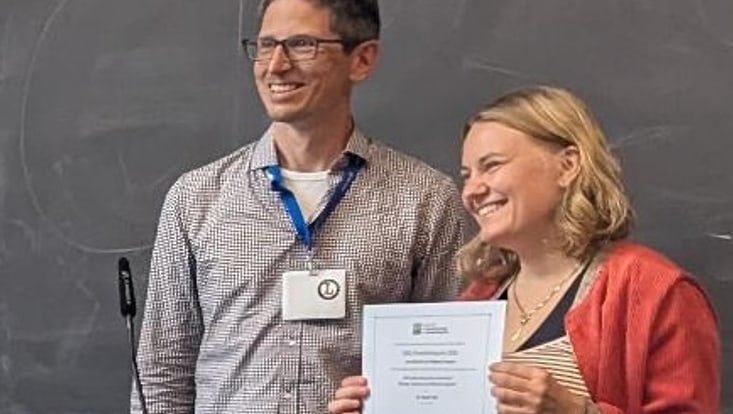 Preisträgerin Neele Falk lächelt und hält ihre Gewinnerurkunde hoch.