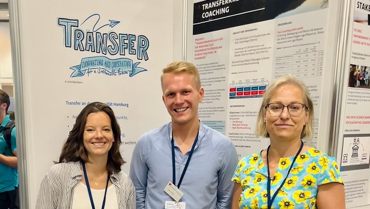Drei Personen vor Plakaten