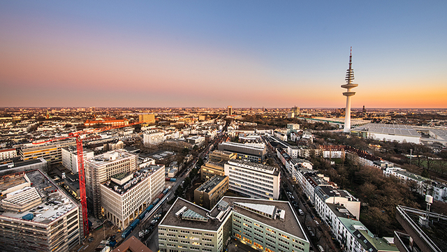 Hamburgs Skyline von oben, es dämmert, der Himmel ist blau mit einem orangenen Schleier.
