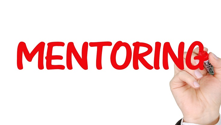 Die Aufschrift Mentoring neben einer Hand mit einem Stift