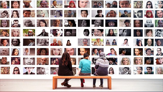 3 Menschen sitzen vor einer Bilderwand mit Gesichtern