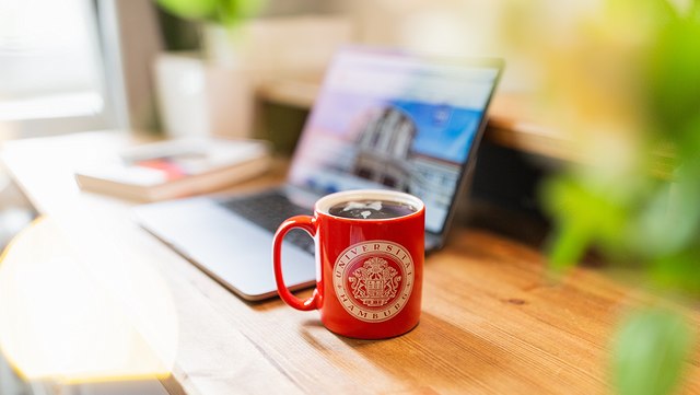Schreibtisch mit Laptop und Kaffeebecher der Uni Hamburg