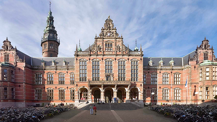 Frontansicht des Hauptgebäudes der Universität Groningen. Imposanter Rotklinkerbau. Auf dem Kopfsteinpflaster-Platz davor stehen unzählige Fahrräder.