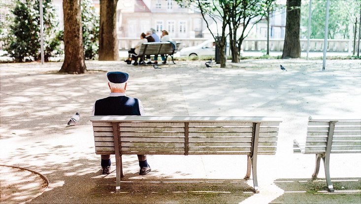 Alter Mensch sitzt einsam auf einer Bank im Park