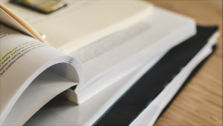 Gestapelte Bücher und Hefter, oberstes liegt geöffnet mit markierter Schrift auf
