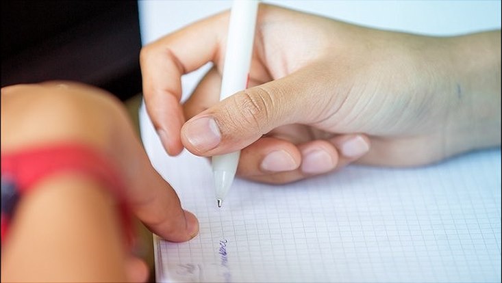 Rechte Hand mit weißem Kugelschreiber schreibt auf weißem karriertem Block