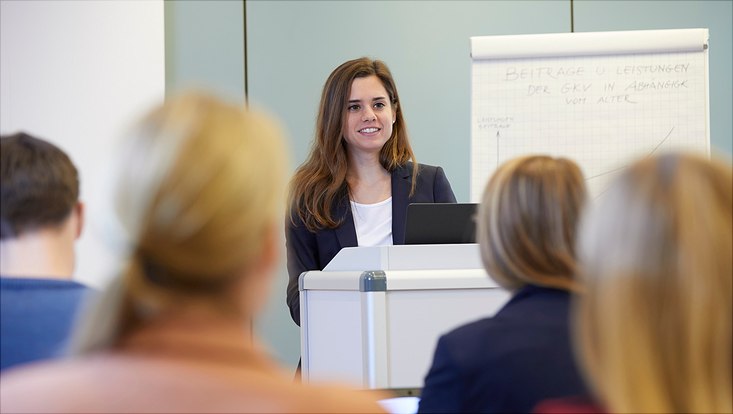 Auf diesem Bild ist Prof. Dr. Eva Oppel am Podium vor einem Publikum zu sehen. Sie erklärt den Zuschauen etwas.