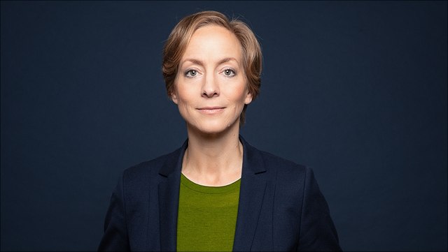 Female with short hair, green shirt and dark blue blazer (Prof. Schröder)